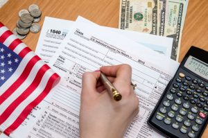 Business woman fills tax form with money, pen, flag,  calculator