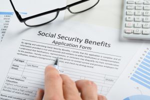 Hand Holding Pen Over Social Security Benefits Form